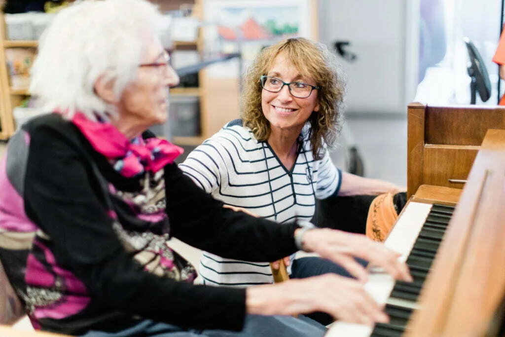 elderly woman plays the piano younger woman listens
